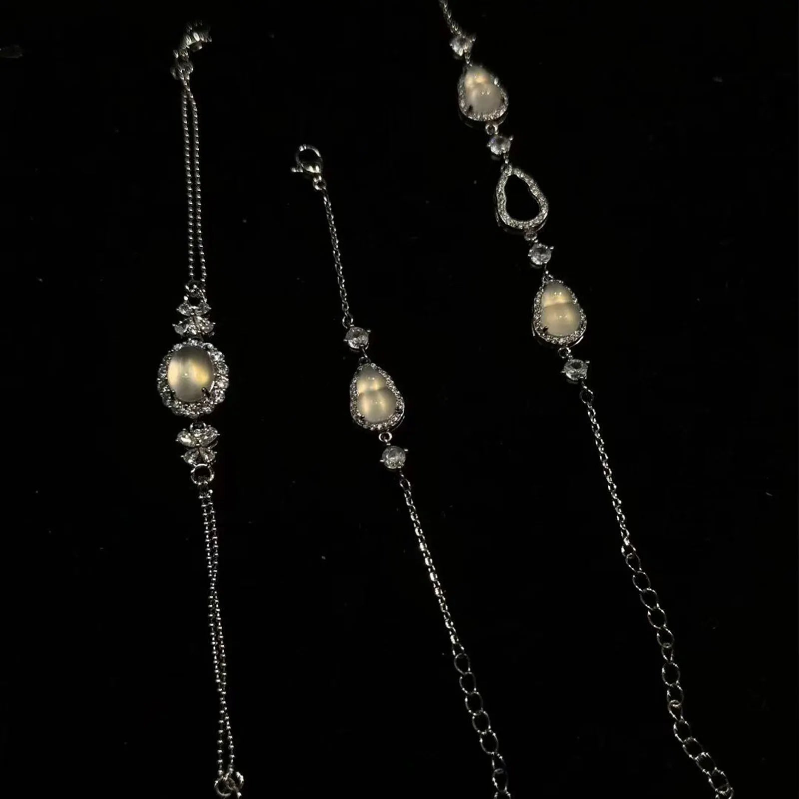 Three elegant silver bracelets adorned with glowing moonstone-like gems (featuring gourd and teardrop shapes) and sparkling crystals, displayed against a dark backdrop — ideal as a complimentary gift.