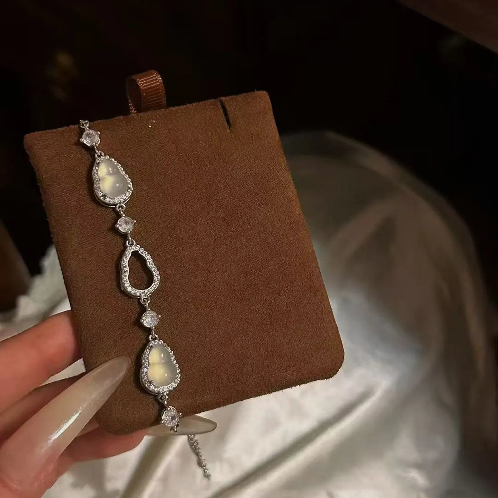 Elegant complimentary crystal bracelet featuring teardrop-shaped luminous stones and sparkling accent details, presented on a brown suede jewelry display.
